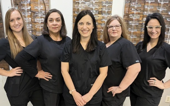 Dr. Tara Bailey with staff members, wearing matching black uniforms standing in front of eyeglass display walls